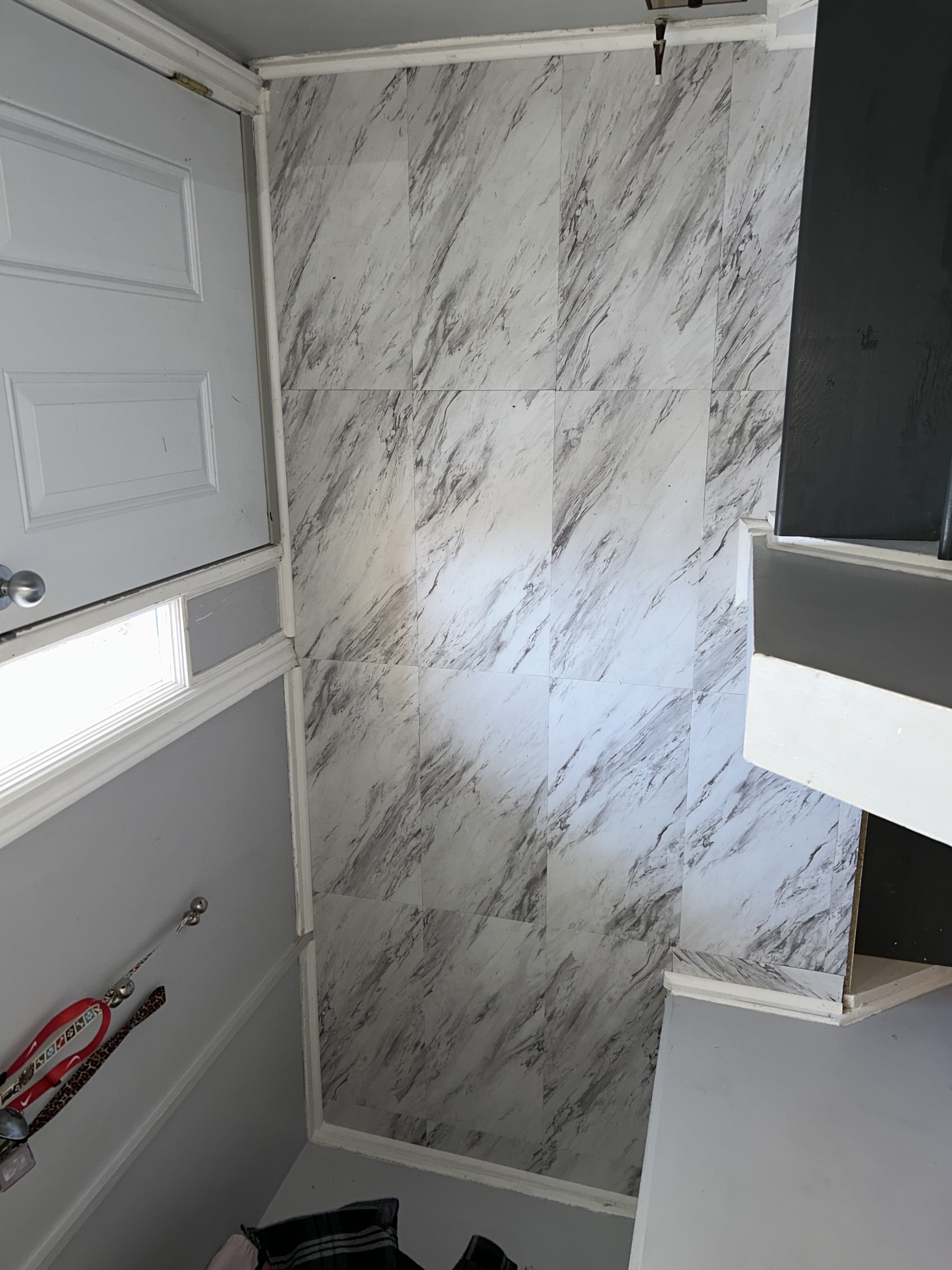 Large-format marble-look tile install on an entryway feature wall, trimmed and cased with painted wood moulding.