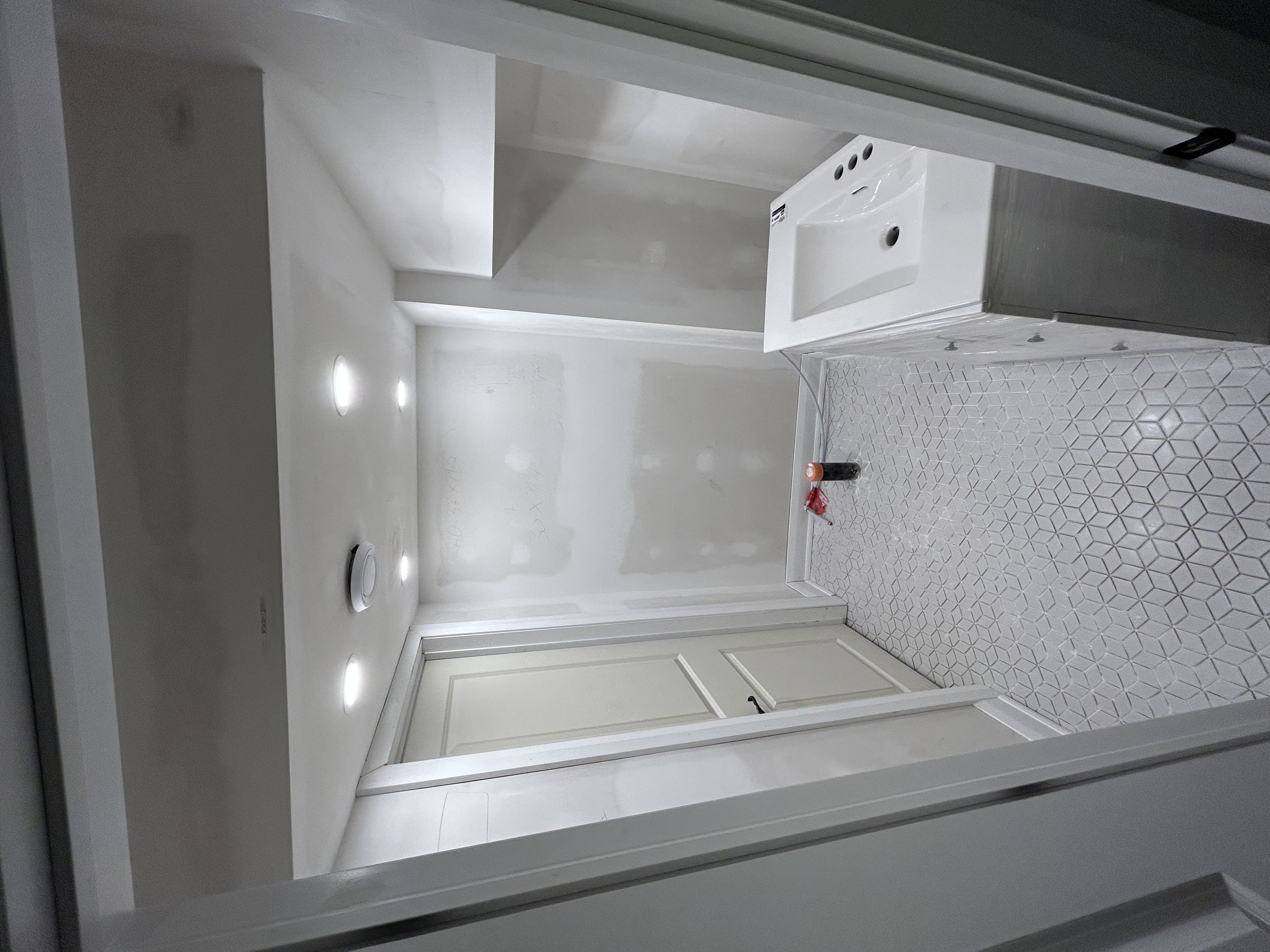 Bathroom rough-in finish work — mosaic tile floor, baseboard, interior door install, drywall finishing, and built-in shelving.